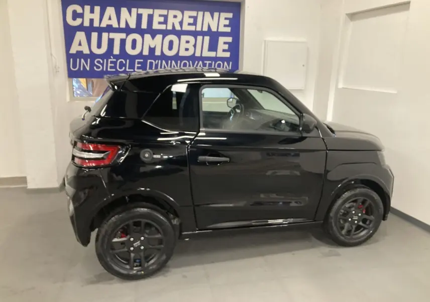 Vue de profil côté gauche d'une Ligier JS50 noire 2026 avec jantes alu noires et feux arrière LED en intérieur showroom.