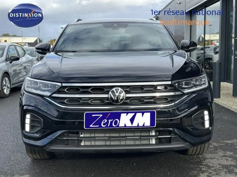 Vue frontale d'un Volkswagen T-Roc 2025 noir Grenadilla métallisé avec calandre hexagonale et feux LED allumés.