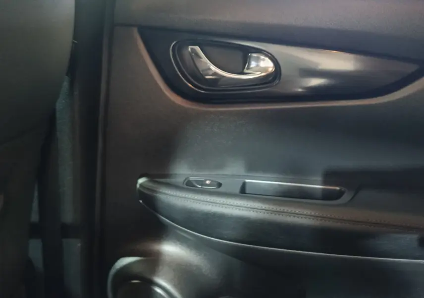 Gros plan sur la poignée intérieure de porte arrière droite du Nissan Qashqai gris clair, avec bouton de verrouillage intégré.