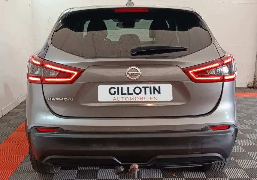 Vue arrière d'un Nissan Qashqai gris clair avec feux LED allumés et attelage visible en intérieur showroom.