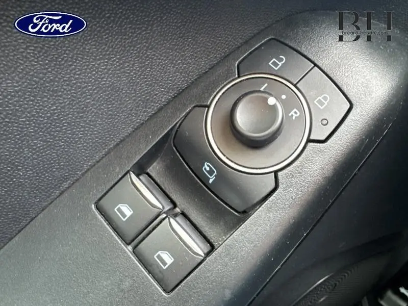 Gros plan sur les commandes de réglage des rétroviseurs et des vitres côté conducteur d'une Ford Fiesta gris lunaire.