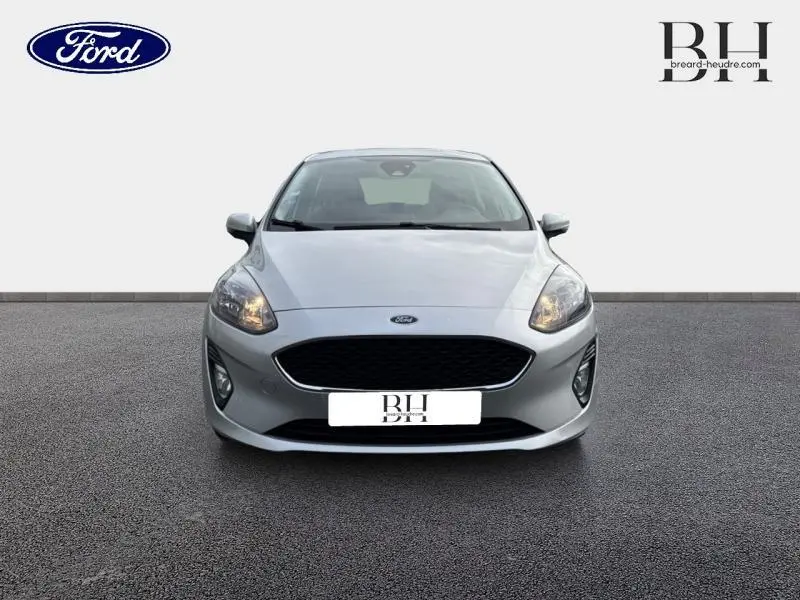 Vue avant d'une Ford Fiesta gris lunaire 2021 avec calandre noire et phares allumés sur fond neutre.