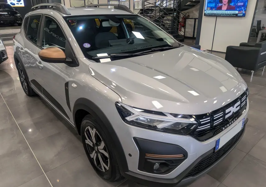 Vue 3/4 avant droit d'une Dacia Sandero Stepway 2023 gris Moonstone avec rétroviseurs bronze et détails noirs contrastants.