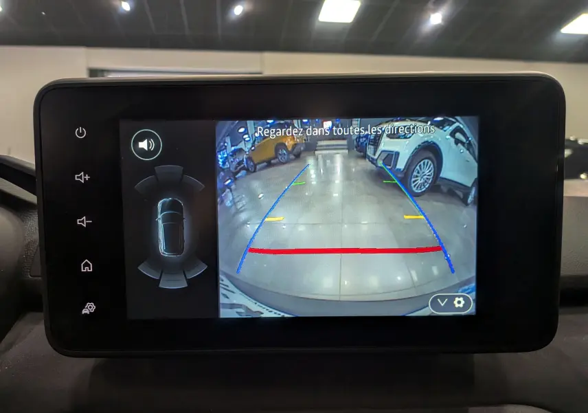Écran de caméra de recul du Dacia Sandero Stepway 2023 montrant l’arrière dans un garage avec plusieurs véhicules visibles.