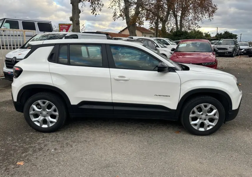 Vue de profil côté gauche d’un Jeep Avenger blanc 2024 avec jantes alliage 17 pouces et protections noires sur bas de caisse.