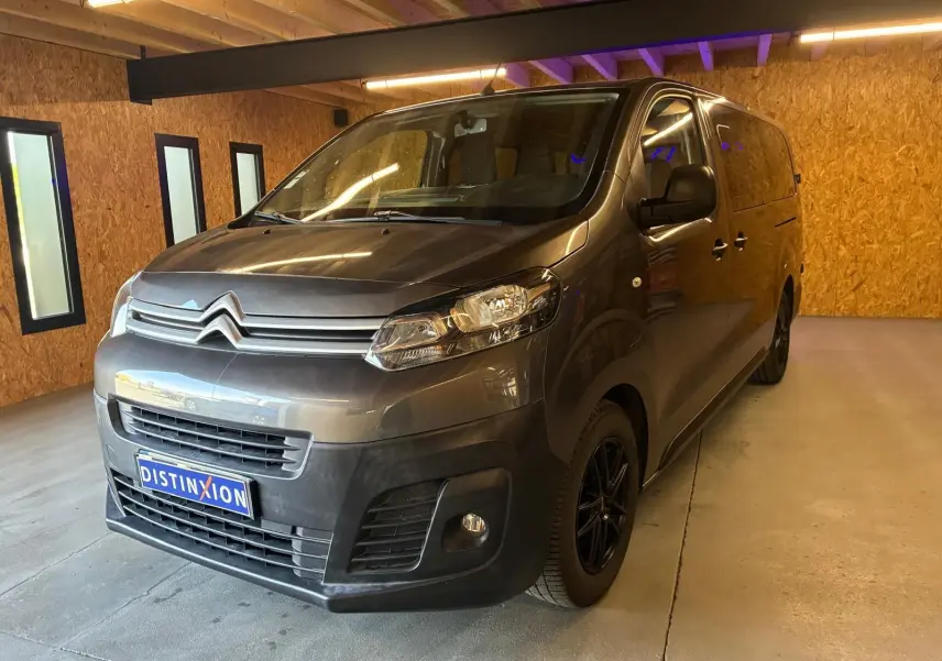 Vue 3/4 avant droit d'un Citroën Jumpy XL Spacetourer gris, avec calandre chromée et jantes noires, en intérieur.