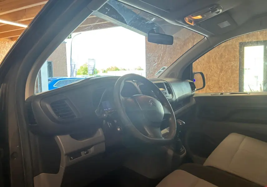 Vue intérieure côté conducteur du Citroën Jumpy gris, montrant le volant, tableau de bord et sièges en tissu.