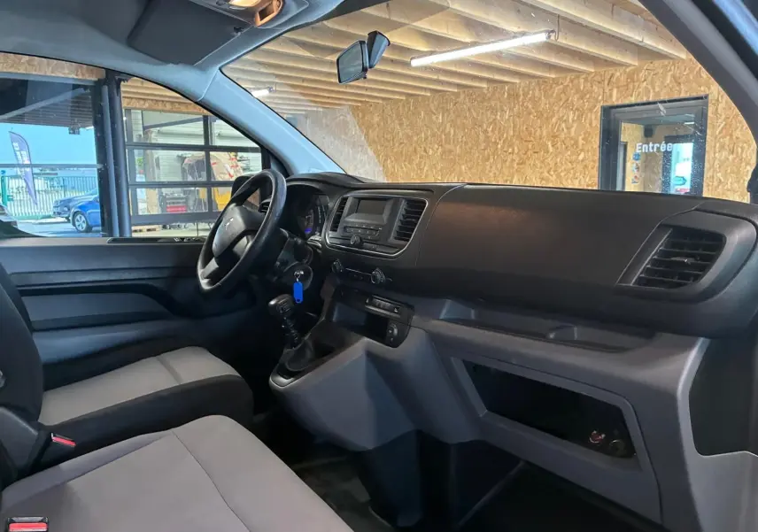Vue intérieure côté conducteur du Citroën Jumpy gris, mettant en valeur le tableau de bord et la boîte manuelle.