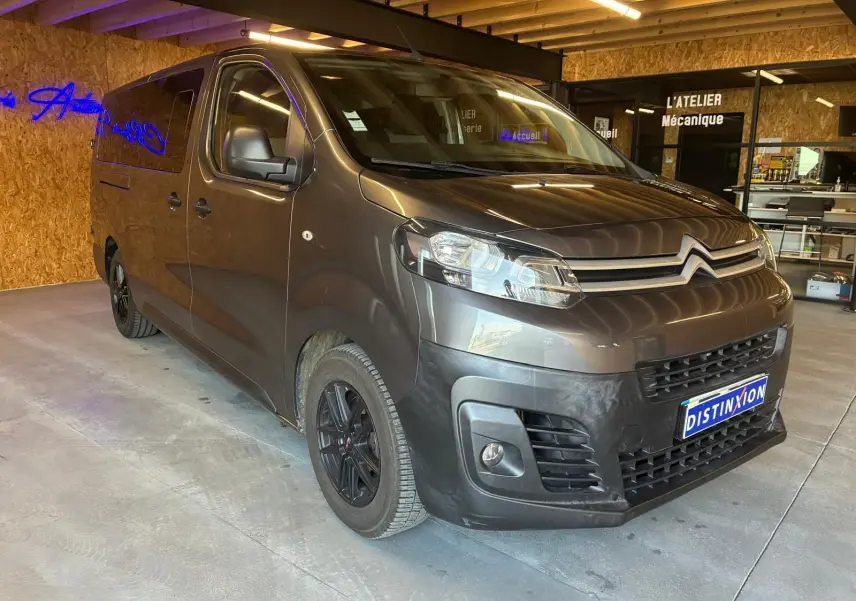 Vue 3/4 avant droit d'un Citroën Jumpy XL Spacetourer gris, avec jantes noires et calandre marquée, en intérieur d'atelier.