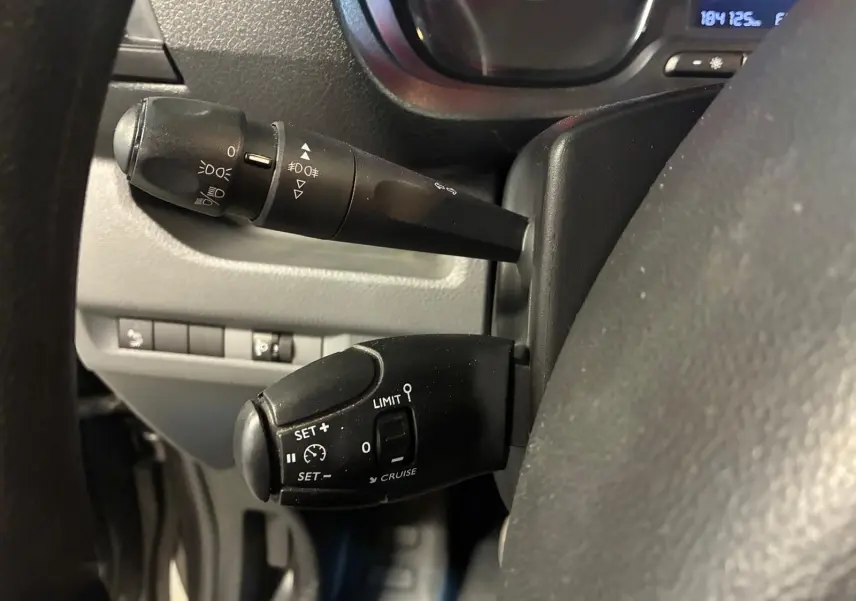 Gros plan sur les commandes de régulateur de vitesse et feux au volant d'un Citroën Jumpy gris, tableau de bord partiel visible.