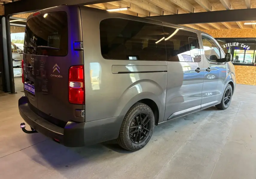 Vue 3/4 arrière droite d’un Citroën Jumpy XL Spacetourer gris avec vitres teintées et jantes noires en intérieur d’atelier.