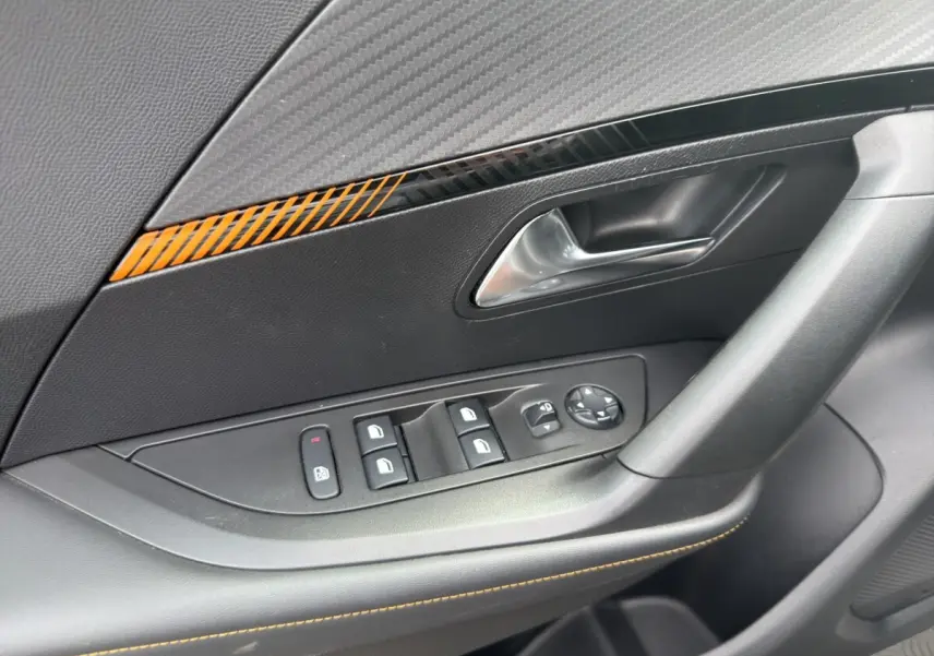 Gros plan sur la porte côté conducteur du Peugeot 2008 gris foncé, avec commandes des vitres et insert décoratif orange.