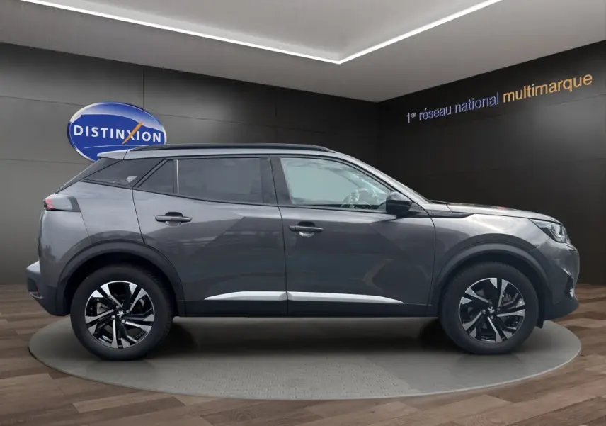 Profil côté droit d'un Peugeot 2008 gris foncé 2022 avec jantes alliage et toit noir en showroom.