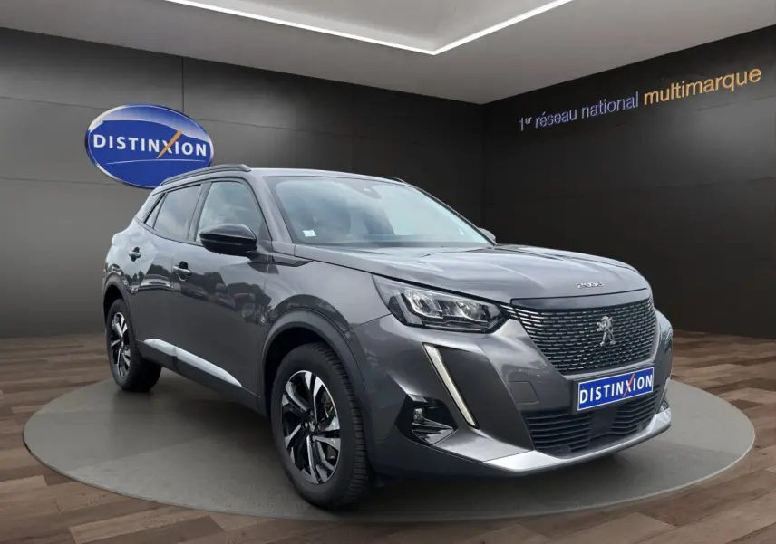 Peugeot 2008 gris foncé en 3/4 avant droit, avec calandre noire et feux LED distinctifs, sur podium intérieur.