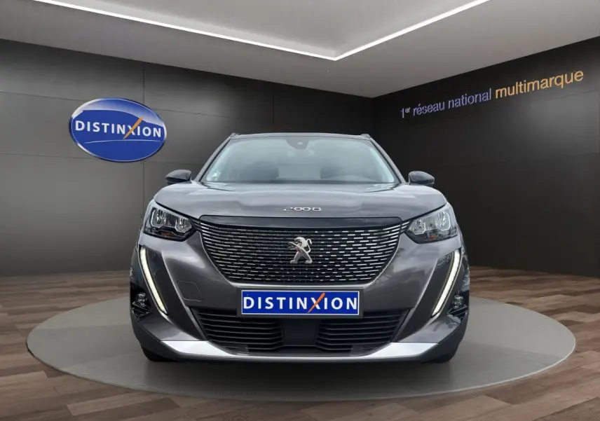 Peugeot 2008 gris foncé vue de face, avec calandre noire et feux LED verticaux allumés en showroom.