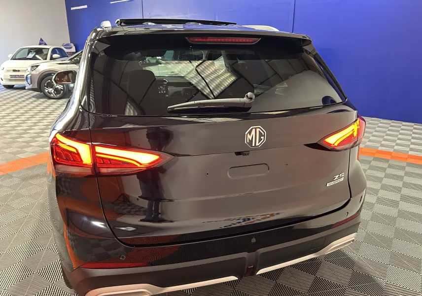 Vue arrière d’un MG MOTOR ZS Hybrid+ 197 Luxury noir Pebble avec feux LED allumés et toit panoramique ouvrant visible.