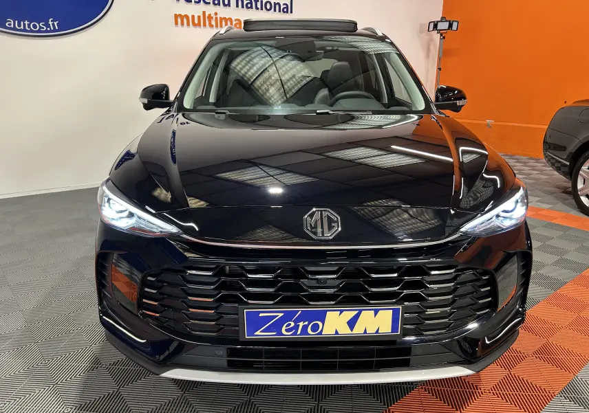 Vue avant du MG ZS Hybrid+ 197 Luxury noir Pebble avec toit panoramique ouvrant et phares LED allumés.