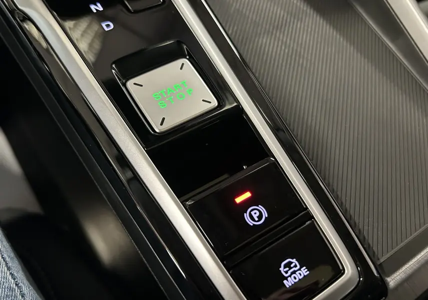 Gros plan sur la console centrale de la MG ZS Hybrid+ 197 Luxury avec bouton Start/Stop vert et commandes de parking et mode.
