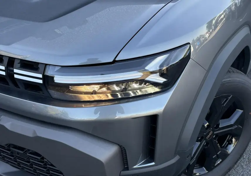 Gros plan sur l'avant droit du Dacia Duster gris schiste, mettant en valeur le phare LED et la jante alliage noire.