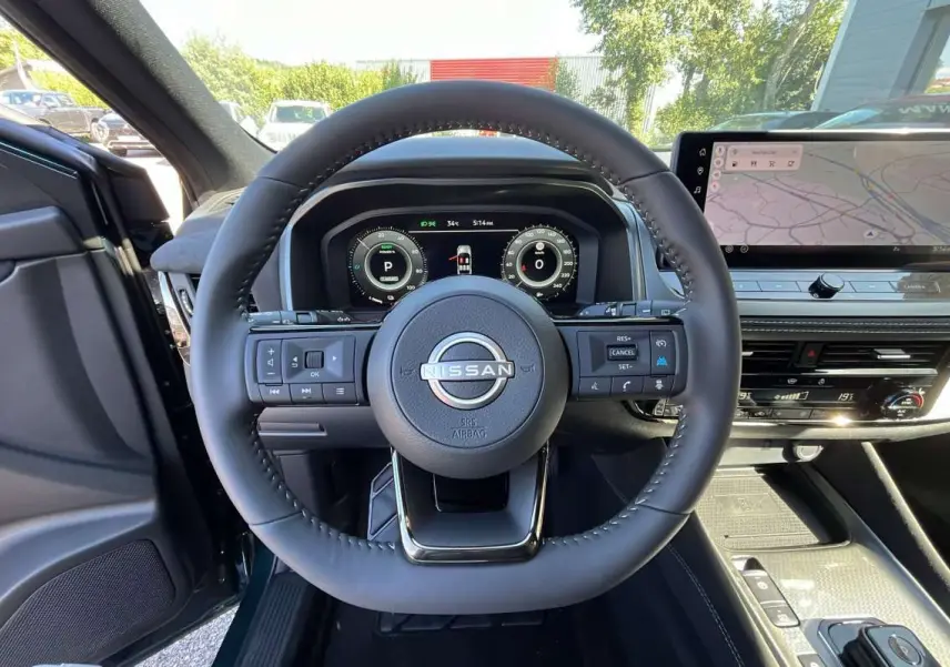 Vue intérieure centrée sur le volant cuir multifonctions du Nissan Qashqai E-POWER 205 N-DESIGN avec écran digital et navigation.