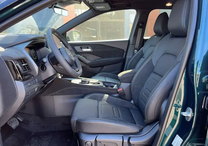 Vue intérieure côté conducteur du Nissan Qashqai E-POWER 205 N-DESIGN 2026, sièges cuir alcantara noirs et portière vert cayuga ouverte.