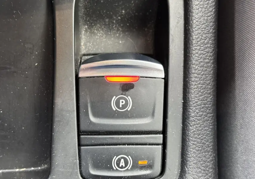 Gros plan sur le bouton du frein de parking électrique activé dans l'habitacle noir de la Renault Clio V 1.0 TCE 100 Initiale Paris.