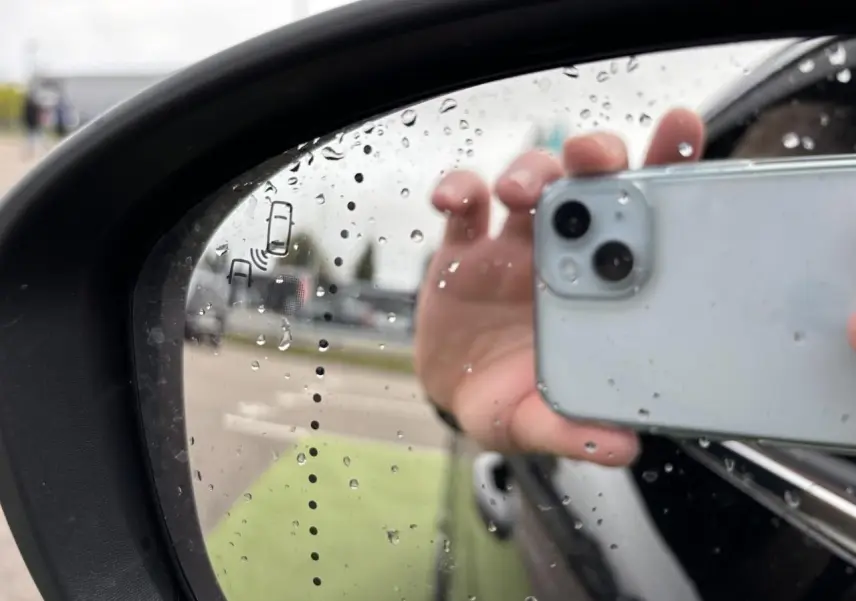 Reflet de la portière noire étoile d'une Renault Clio 2020 dans le rétroviseur côté gauche sous la pluie.