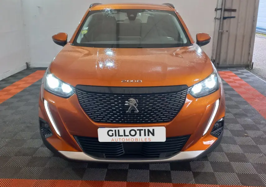 Peugeot 2008 orange vue de face, phares LED allumés et calandre noire avec logo lion visible.