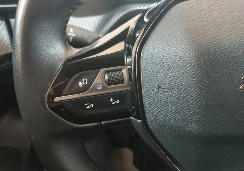 Gros plan sur la partie gauche du volant cuir noir du Peugeot 2008 orange, avec commandes vocales et volume.