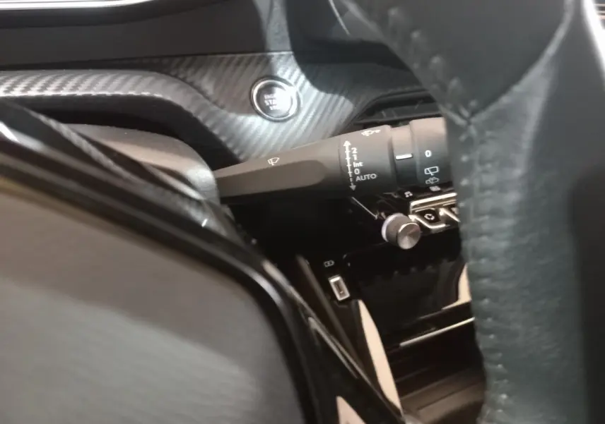 Gros plan sur la commande d’essuie-glace et bouton démarrage dans l’habitacle noir du Peugeot 2008 orange.