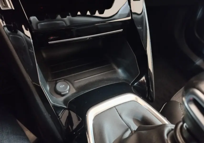 Gros plan sur la console centrale noire brillante avec prise 12V et levier de vitesse en cuir du Peugeot 2008 orange.
