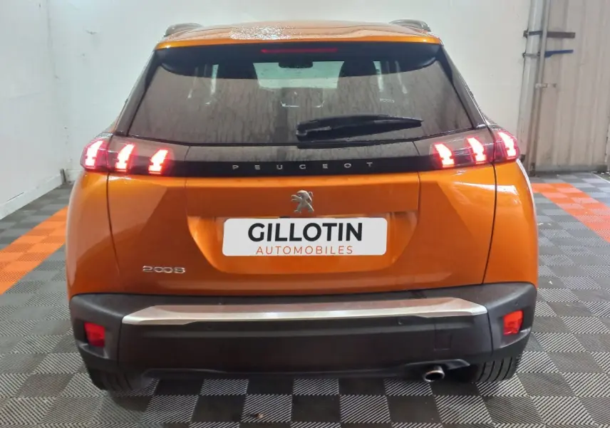 Vue arrière d'un Peugeot 2008 orange avec feux arrière allumés et logo lion visible sur le hayon.
