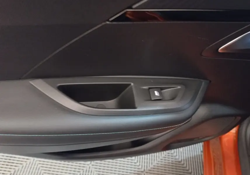 Gros plan sur la porte côté droit d'une Peugeot 2008 orange, montrant la commande de lève-vitre et le revêtement noir.
