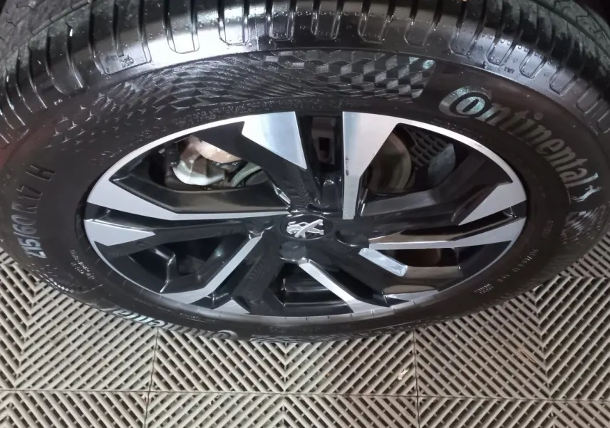 Gros plan sur la jante alliage noire et argentée avec logo Peugeot, montée d'un pneu Continental.