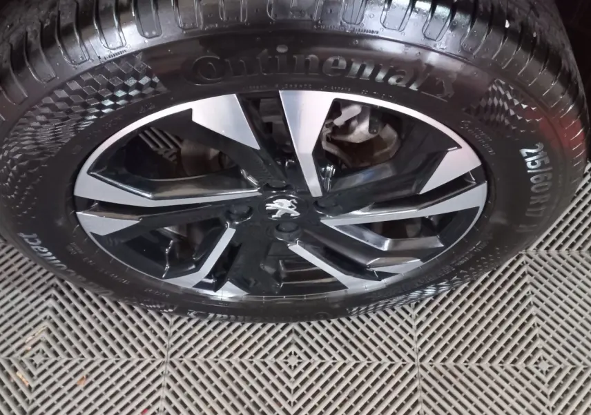 Gros plan sur la jante alliage noire et argentée avec logo Peugeot, montée d'un pneu Continental sur Peugeot 2008 orange.