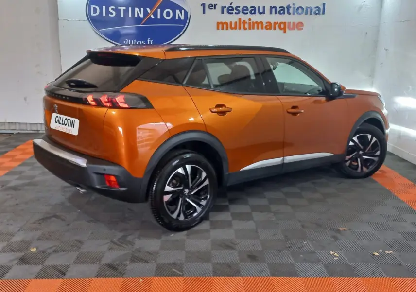 Peugeot 2008 orange vue 3/4 arrière droit en intérieur, avec jantes noires et toit noir contrasté.