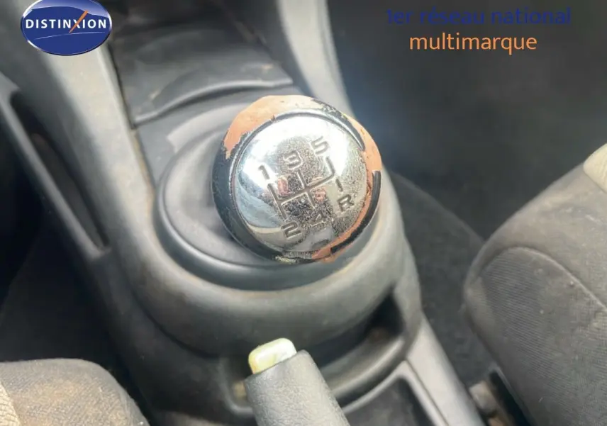 Gros plan sur le levier de vitesse manuel usé de la Citroën C4 Coupé noir métal de 2009, intérieur tissu gris visible.