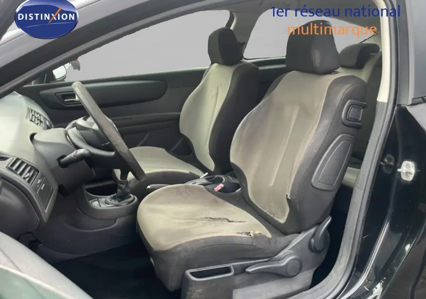 Vue intérieure côté gauche montrant les sièges avant gris tissu et volant d'une Citroën C4 Coupé noir métal 2009.