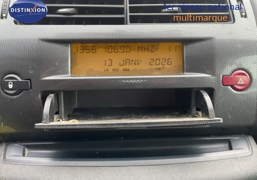 Vue rapprochée du tableau de bord de la Citroën C4 Coupé 2009, affichage radio orange et bouton rouge d'alerte visible.