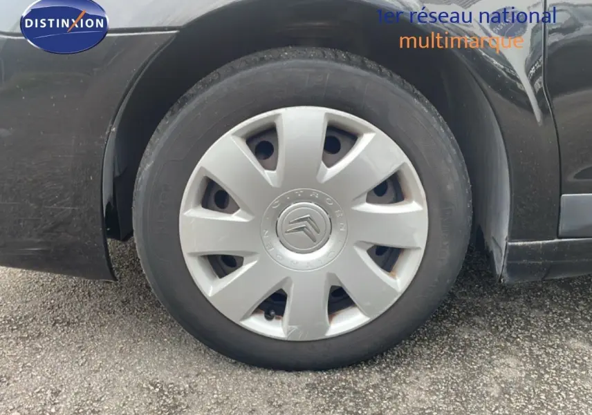 Gros plan sur la roue avant gauche d'une Citroën C4 Coupé 2009 noir métal avec enjoliveur gris.