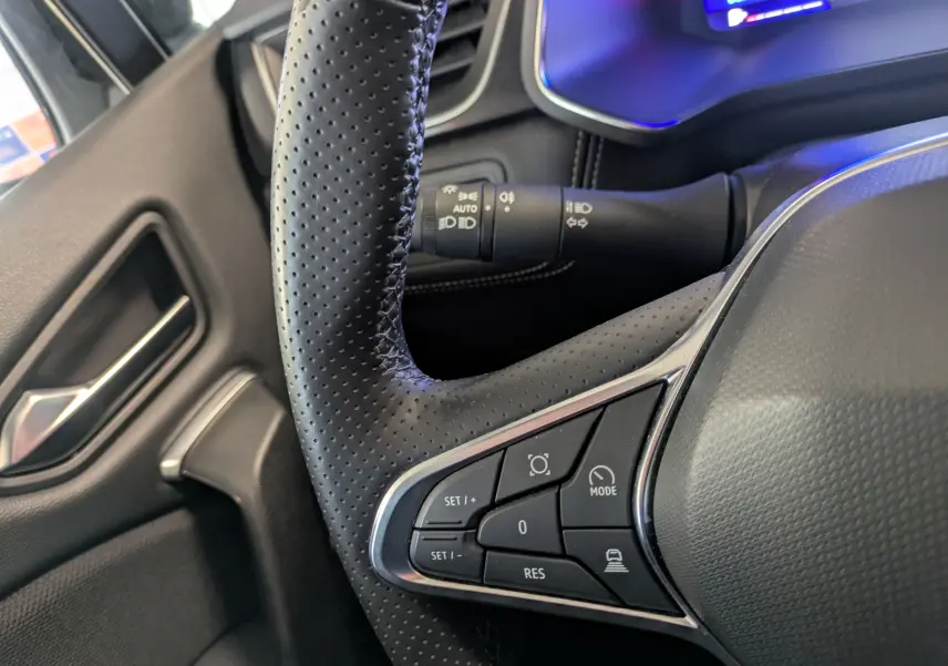 Gros plan sur le volant en cuir perforé côté gauche du Renault Symbioz gris cassiopée, avec commandes intégrées et tableau de bord partiellement visible.