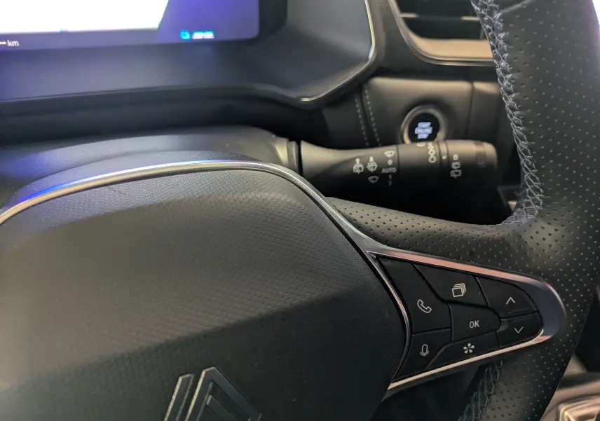Gros plan sur le volant noir perforé avec commandes intégrées et tableau de bord numérique du Renault Symbioz gris Cassiopée.