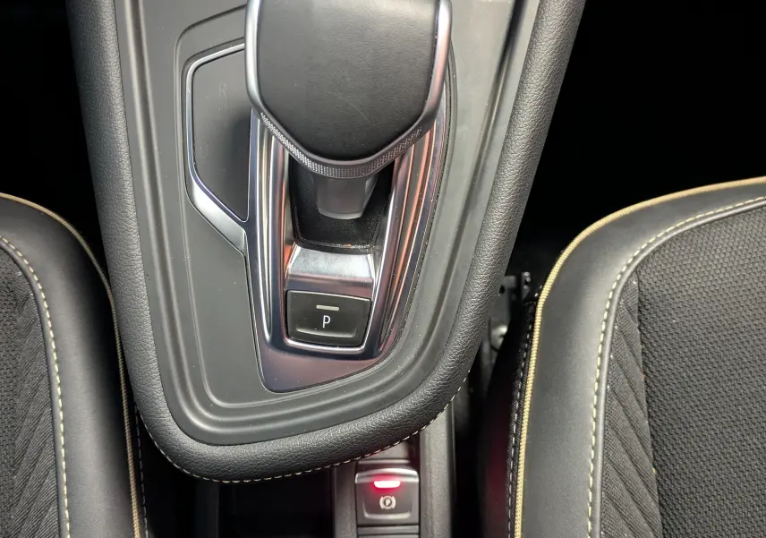 Vue plongeante sur la console centrale du Renault Symbioz 2025, levier de boîte auto noir et sièges tissu noir avec surpiqûres beige.