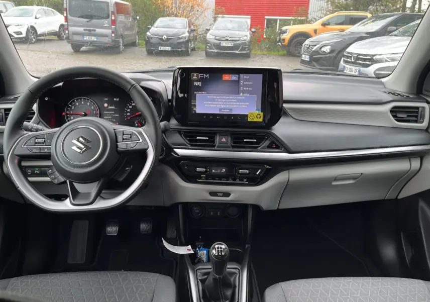 Vue intérieure avant du Suzuki Swift 2026 gris, volant cuir multifonctions et écran tactile central avec boîte manuelle.
