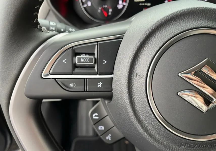 Gros plan sur le volant cuir gris de la Suzuki Swift 2026, avec commandes multifonctions et logo Suzuki central chromé.