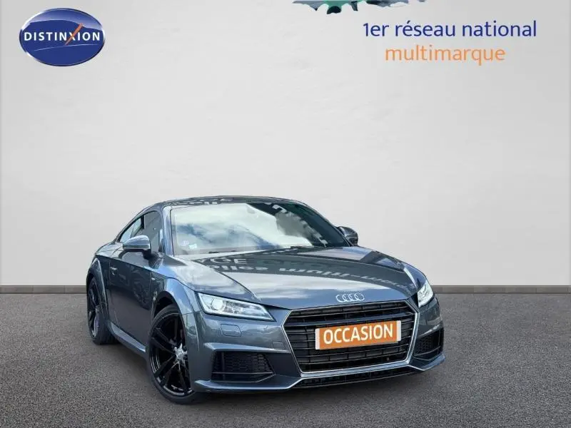 Audi TT Coupé gris métallisé en 3/4 avant avec jantes noires et plaque orange "OCCASION" visible sur un fond neutre.