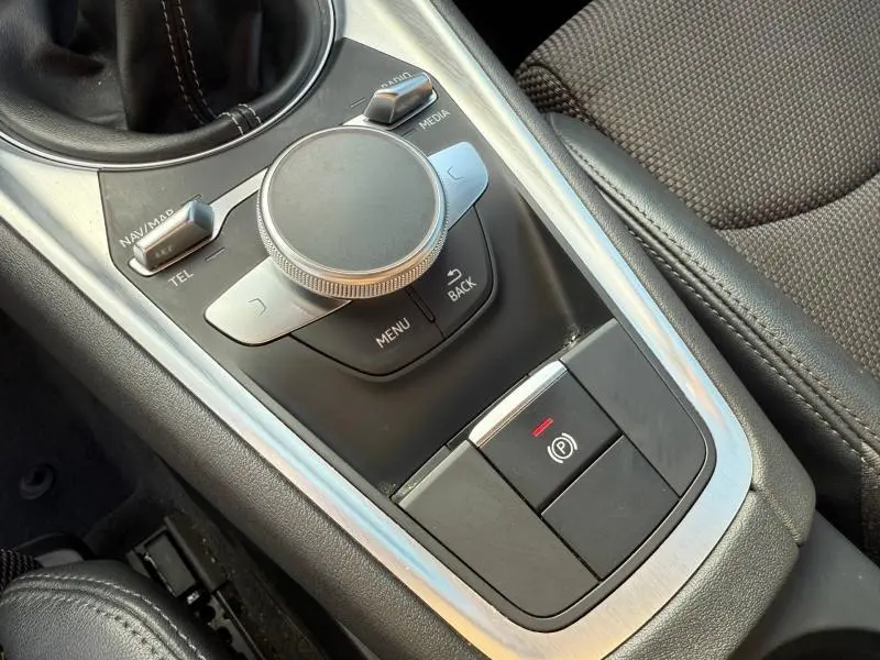 Vue rapprochée de la console centrale noire et argentée de l'Audi TT Coupé 2016 avec commandes multimédia et frein à main électrique.