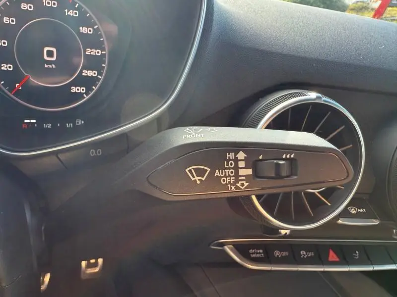 Gros plan sur le commodo d’essuie-glace noir et la sortie d’air circulaire argentée dans l’habitacle sombre d’une Audi TT Coupé 2016.
