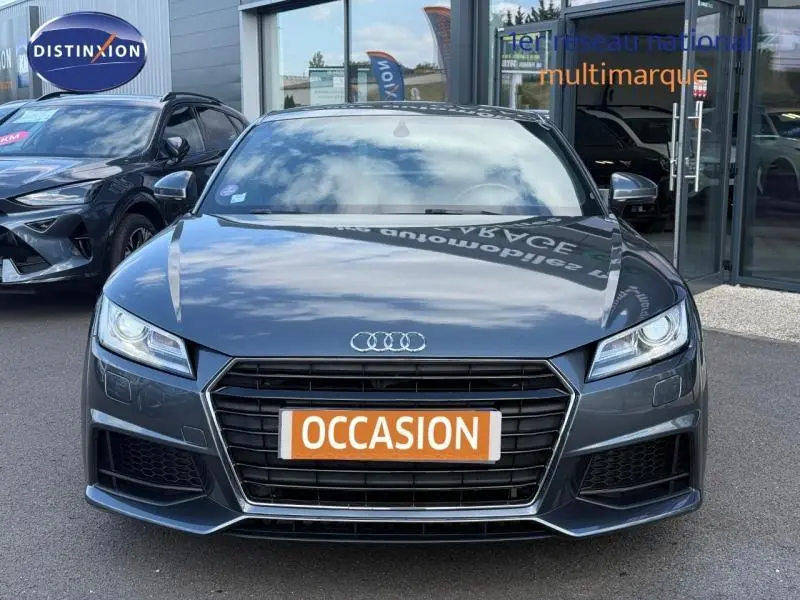 Vue frontale d'une Audi TT Coupé gris métallisé avec calandre noire et plaque "OCCASION" orange.