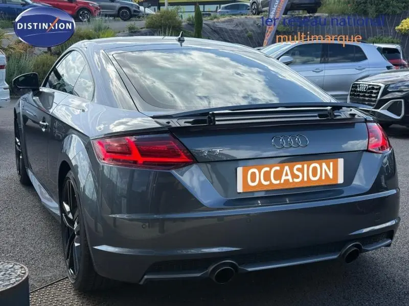 Vue 3/4 arrière d’une Audi TT Coupé gris foncé avec becquet arrière et double sortie d’échappement chromée.